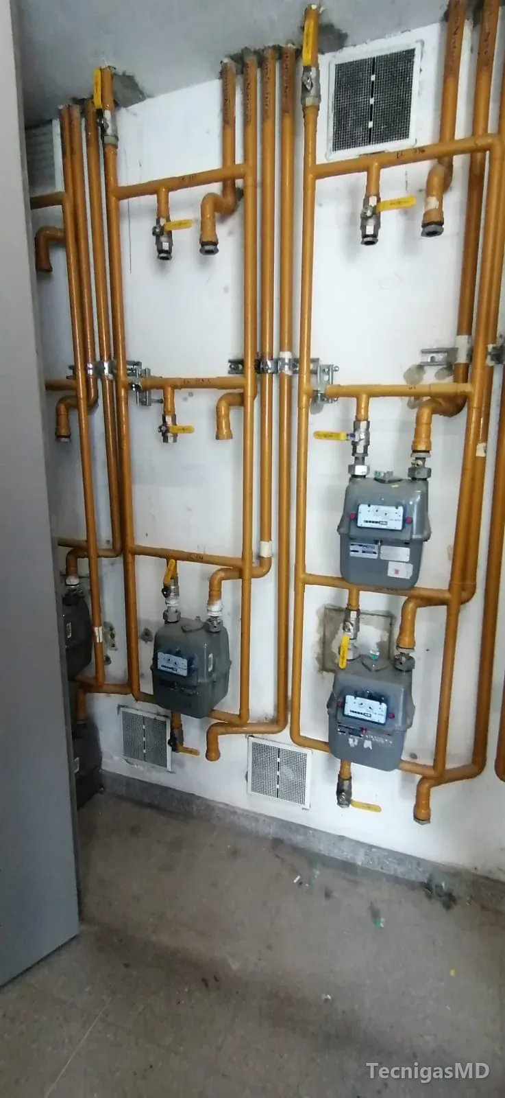 Centro de medición con medidores de gas natural, tubería amarilla, válvulas de corte y rejillas de ventilación en el muro