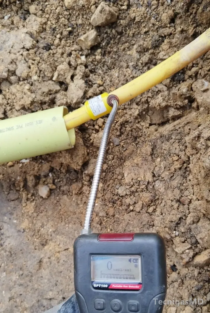 Detector portátil de gas con lectura en cero midiendo en la unión de una tubería amarilla de acometida dentro de una zanja
