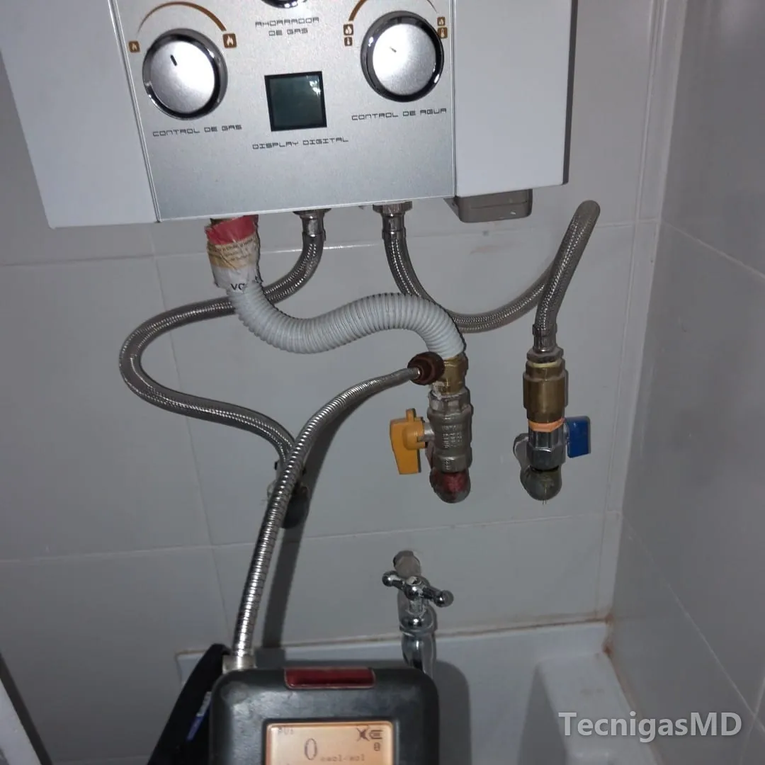 Detector de gas midiendo en la unión del tubo corrugado con la llave de manija amarilla bajo un calentador de paso