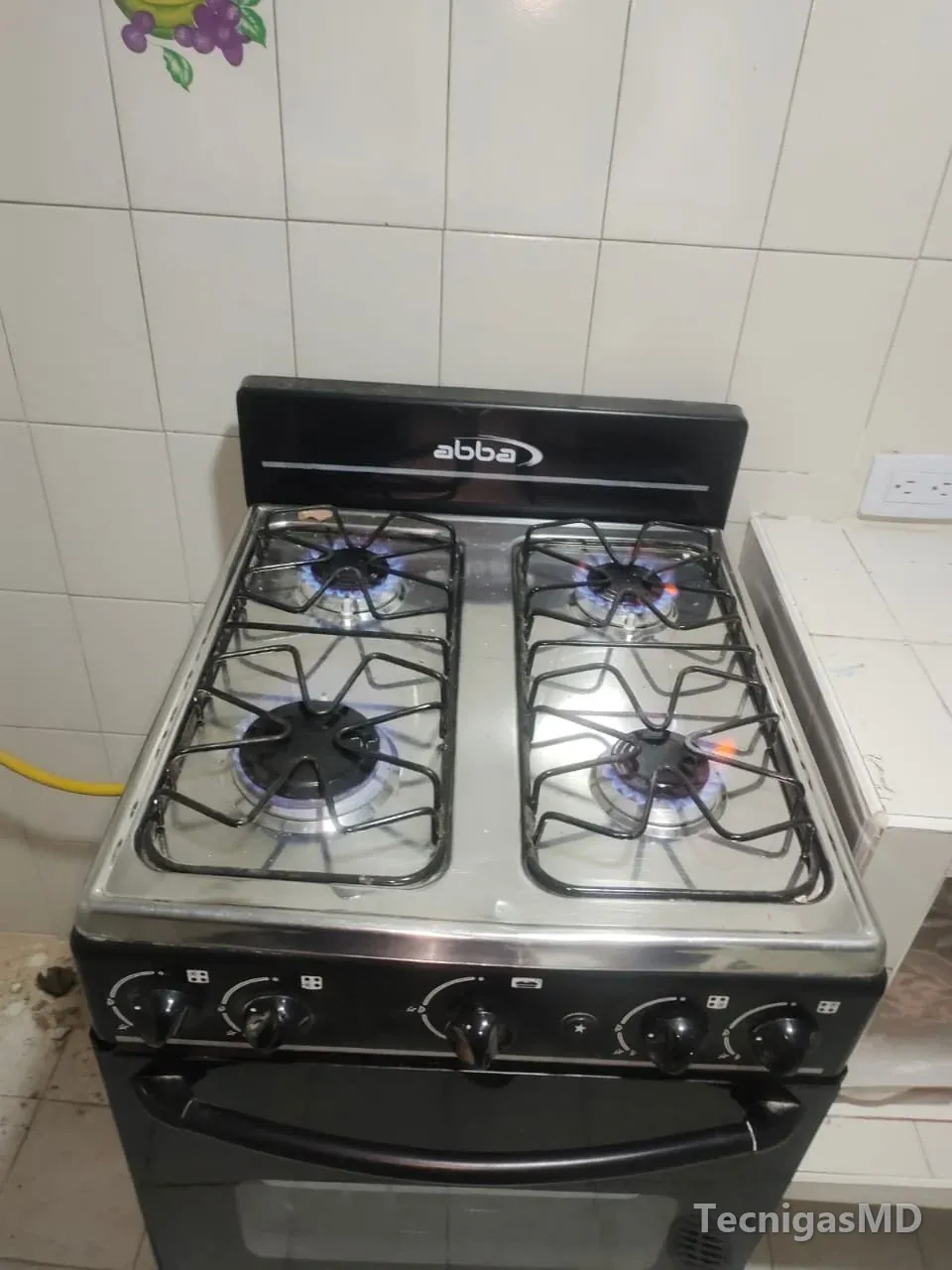 Estufa de piso abba a gas con cuatro quemadores en llama azul, horno inferior y manguera amarilla de gas al costado