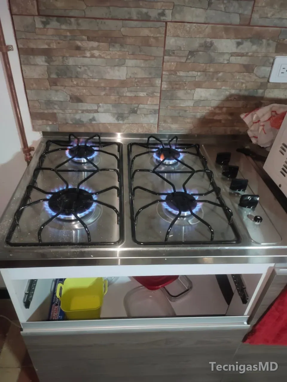 Estufa a gas de cuatro quemadores sobre mueble de cocina, con todos los puestos encendidos y llama azul