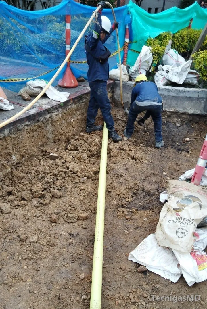 Dos técnicos con casco trabajan en una excavación donde se tiende tubería amarilla para acometida de gas natural