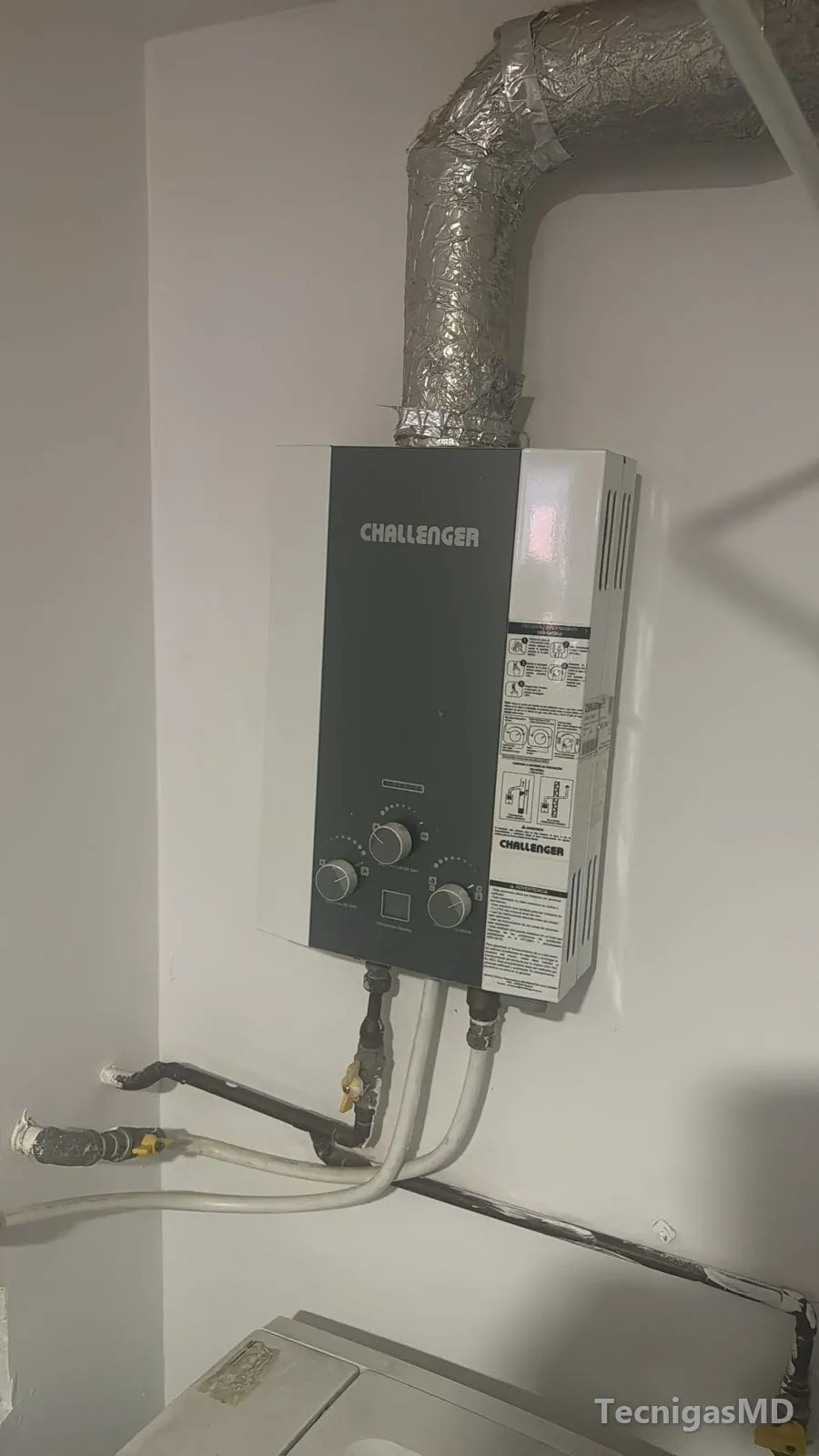 Calentador a gas de paso Challenger instalado en muro, con ducto de evacuación en aluminio y conexiones de agua y gas