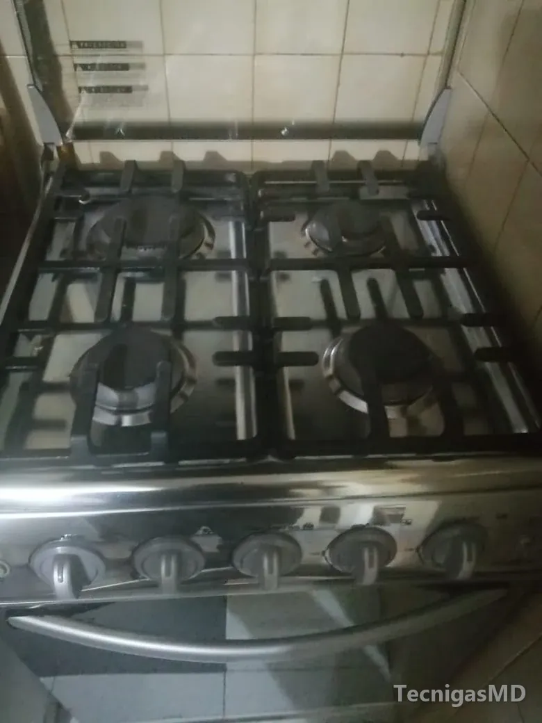 Estufa de piso a gas en acero inoxidable con cuatro quemadores, parrillas negras, perillas frontales y horno