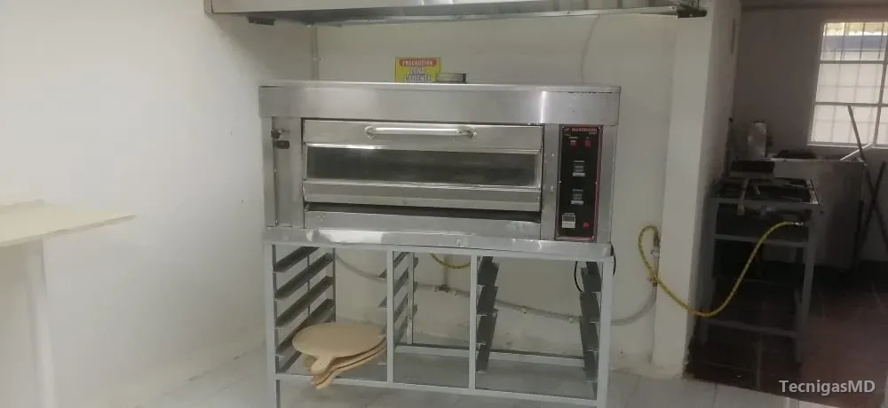 Horno industrial a gas de acero inoxidable con panel digital, sobre base con bandejero y bajo una campana extractora