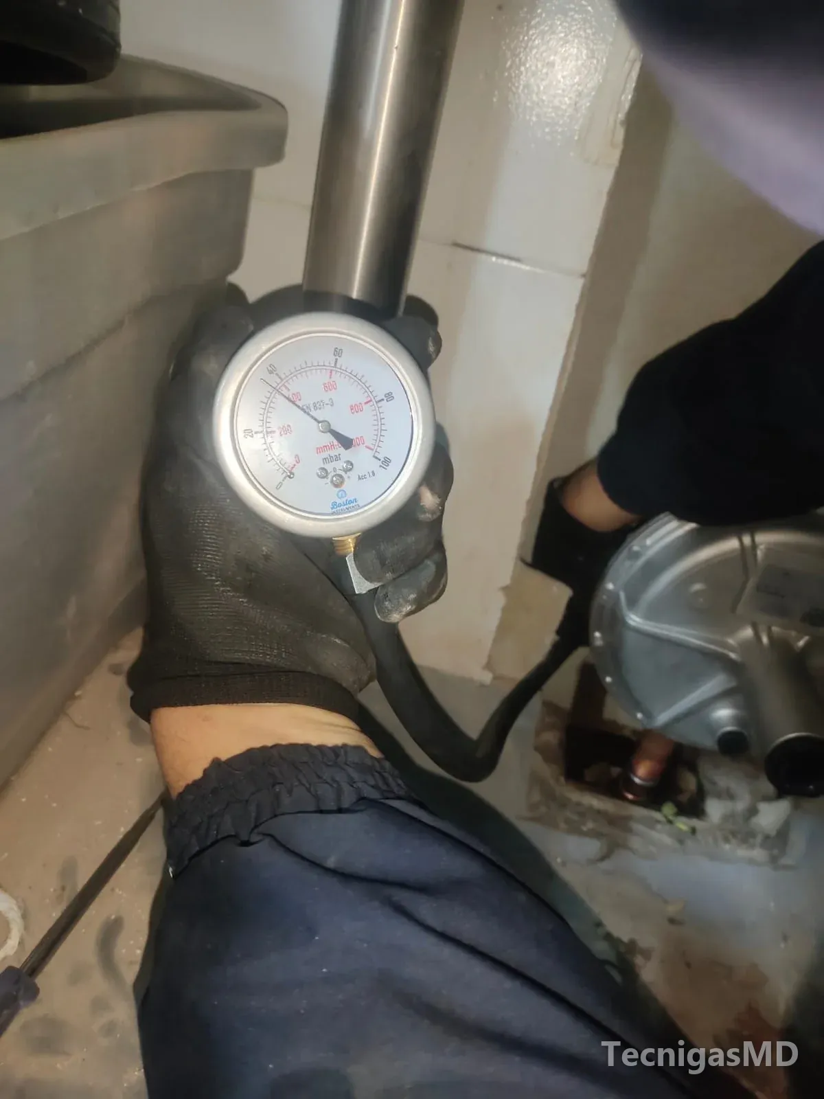 Técnico con guantes sosteniendo un manómetro conectado por manguera a la red de gas natural, junto a un regulador