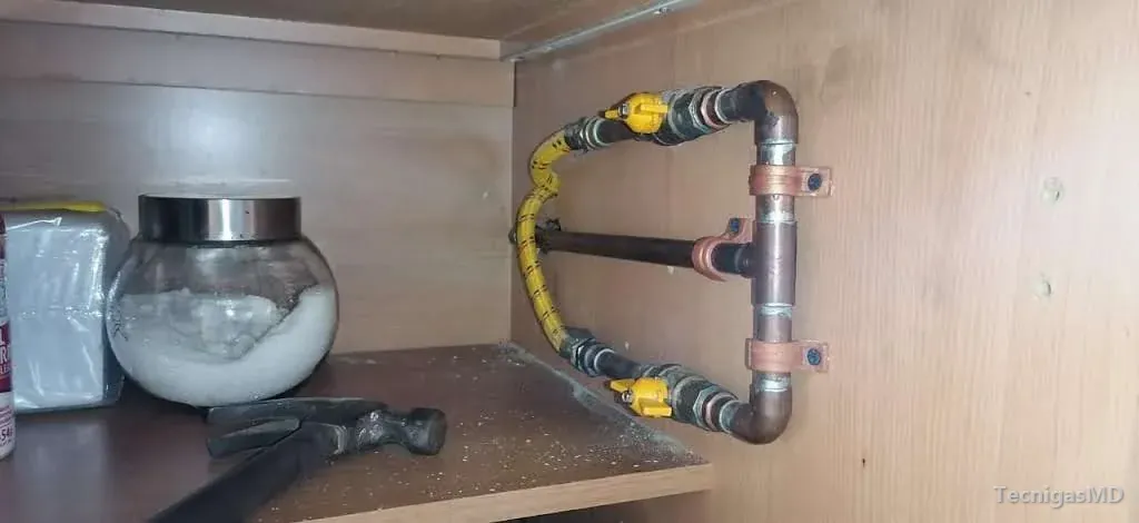 Tubería de cobre con abrazaderas dentro de un mueble de madera, con dos válvulas de manija amarilla y manguera flexible