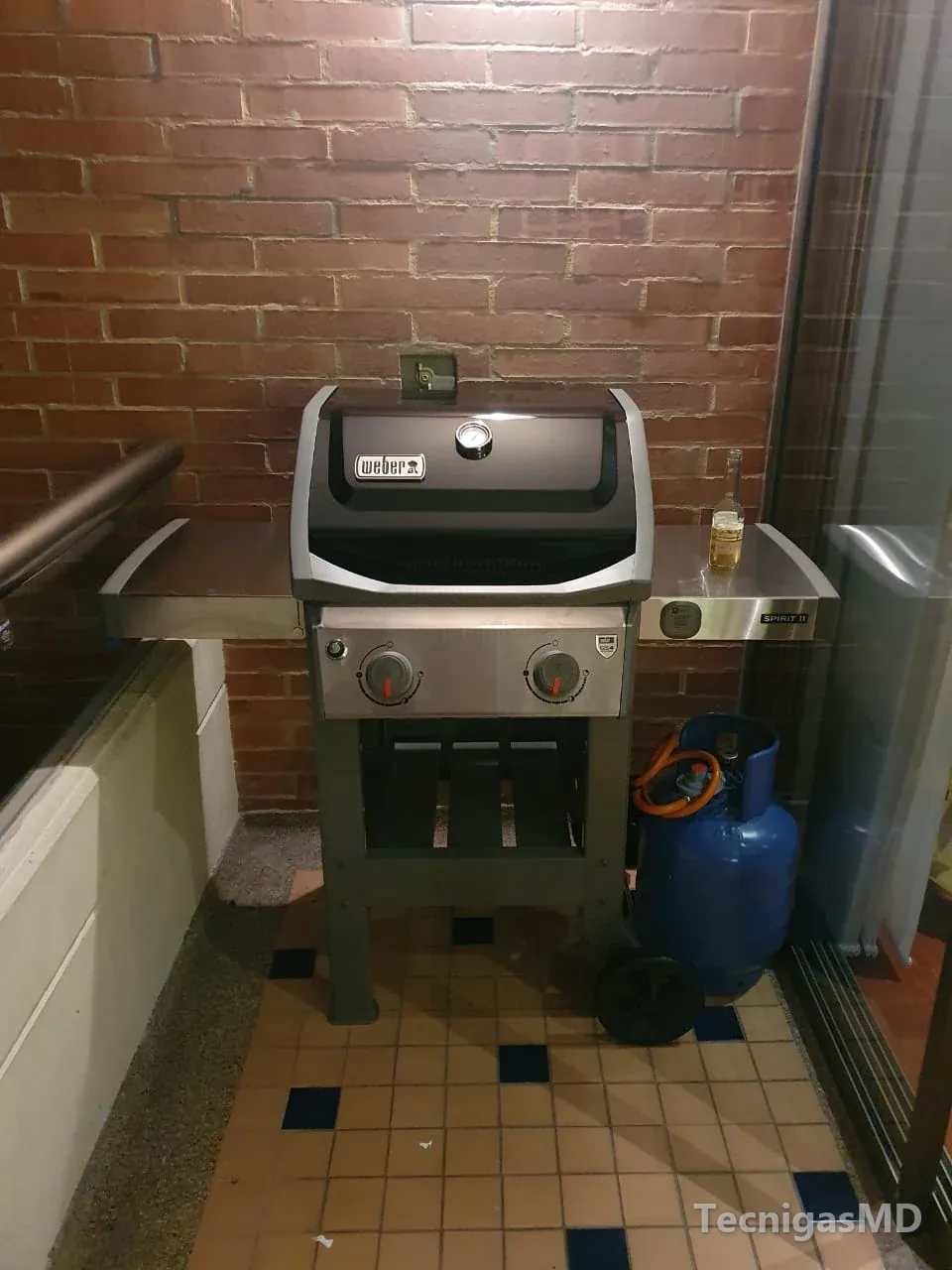 Asador a gas en un balcón con muro de ladrillo y, detrás, la caja empotrada con la válvula del punto de gas