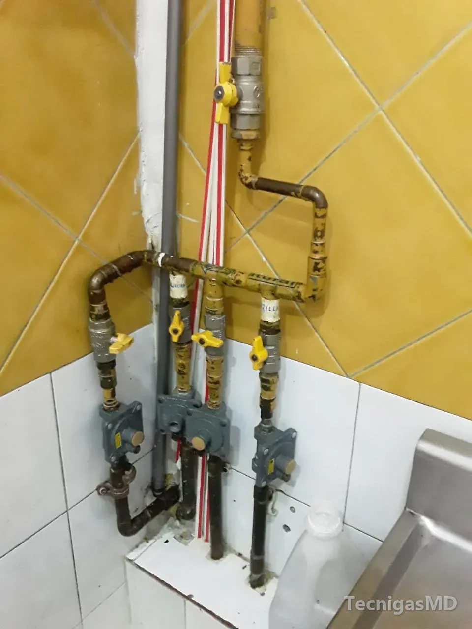 Red de gas natural en tubería amarilla con cuatro salidas, cada una con válvula de corte y regulador, sobre muro enchapado