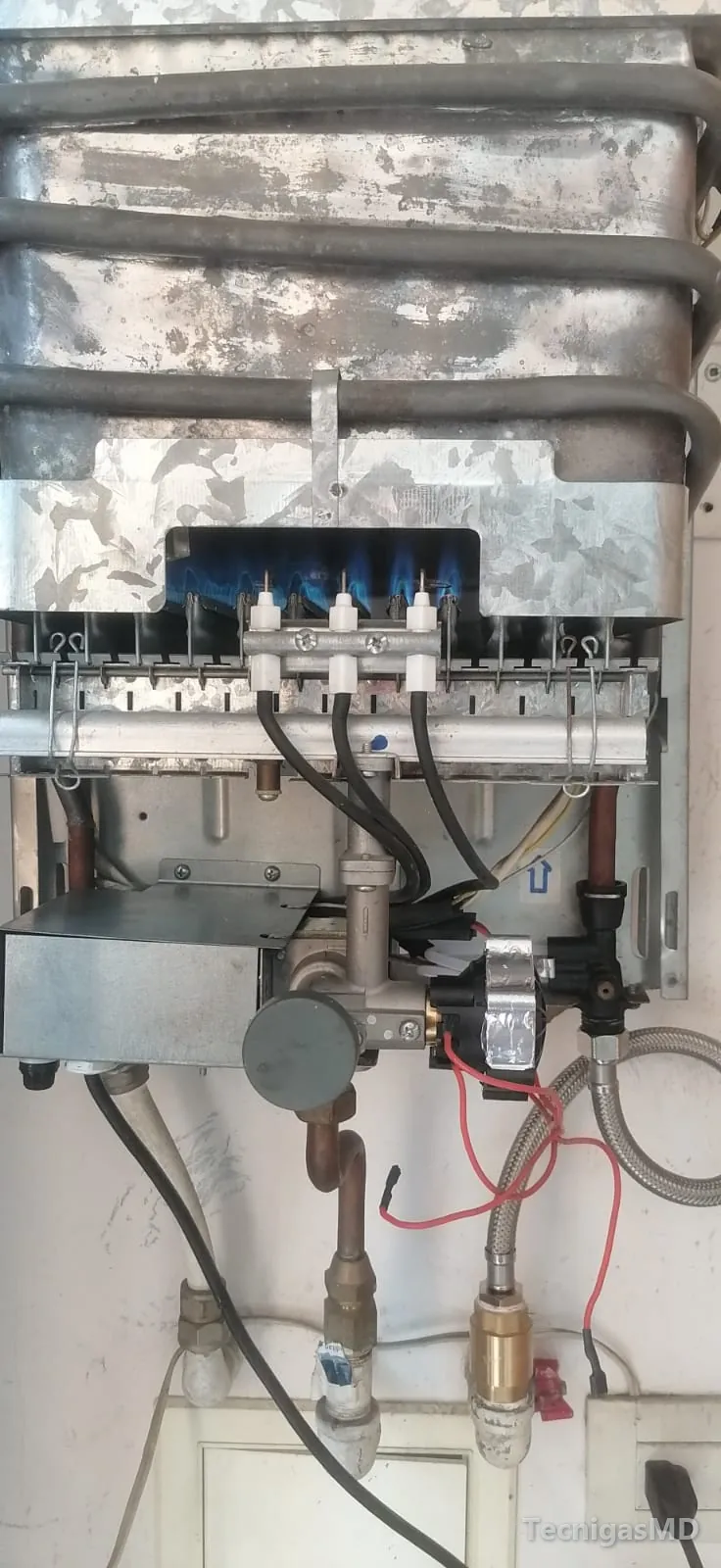 Calentador a gas de paso sin carcasa con el quemador encendido y los electrodos, la válvula y el intercambiador a la vista