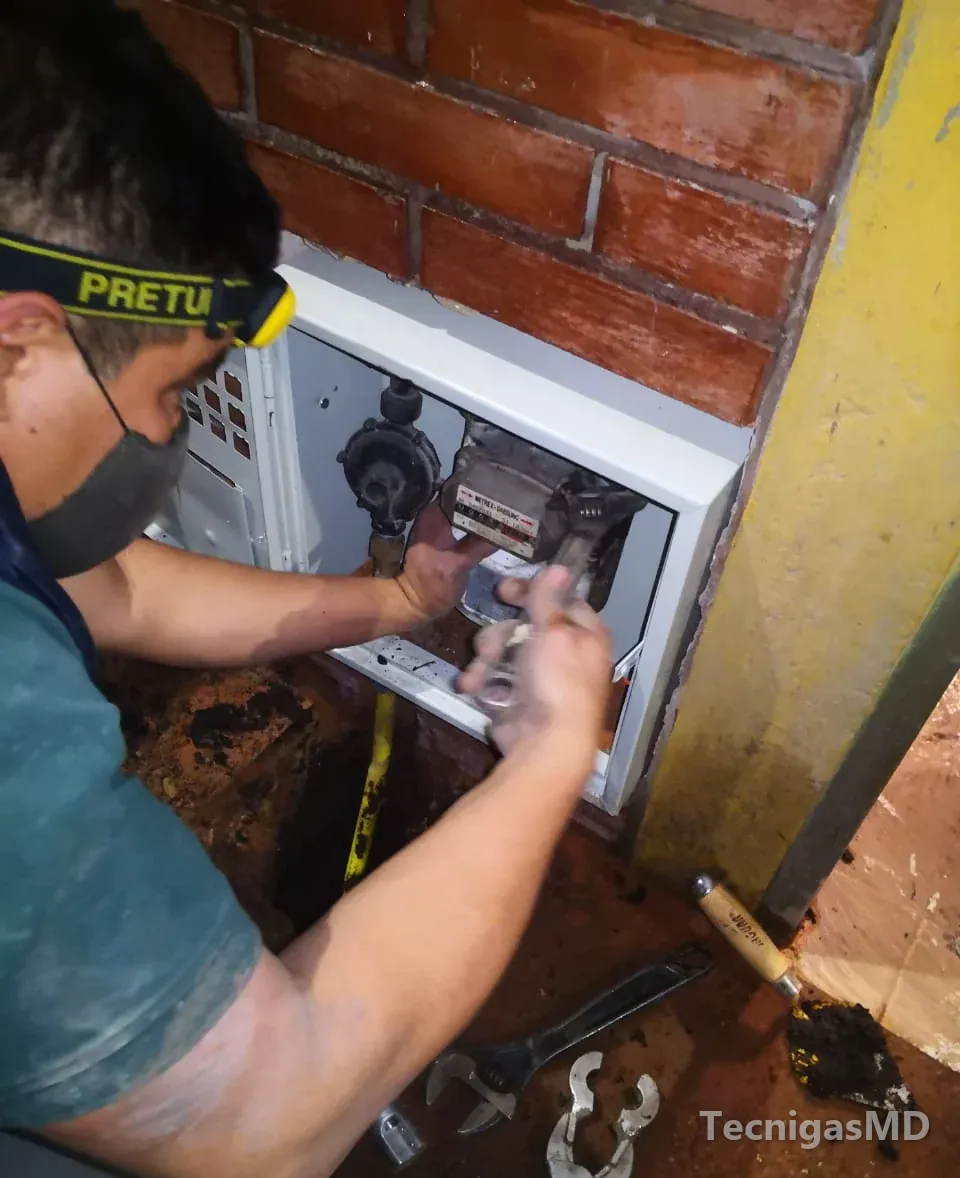 Técnico de TecnigasMD ajustando con llave el medidor y el regulador de gas natural dentro de un gabinete en muro de ladrillo