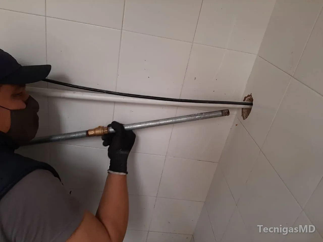 Técnico con guantes pasa tubería metálica de red interna de gas natural por una perforación en un muro enchapado