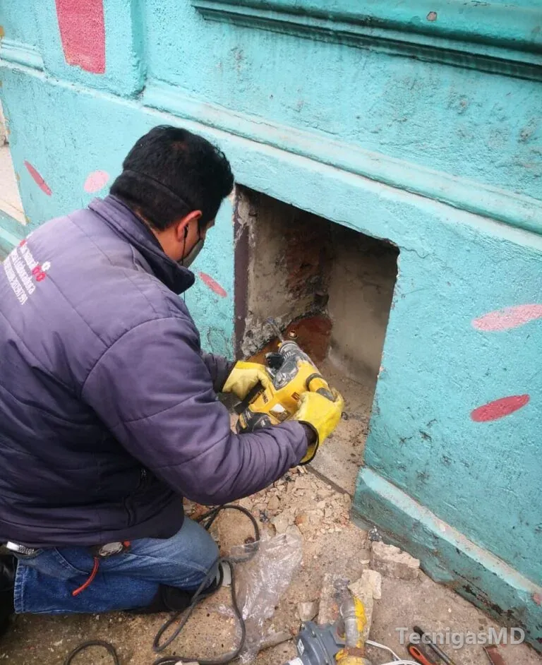 Técnico de TecnigasMD con guantes y tapabocas picando con herramienta eléctrica un nicho abierto en la base de una fachada