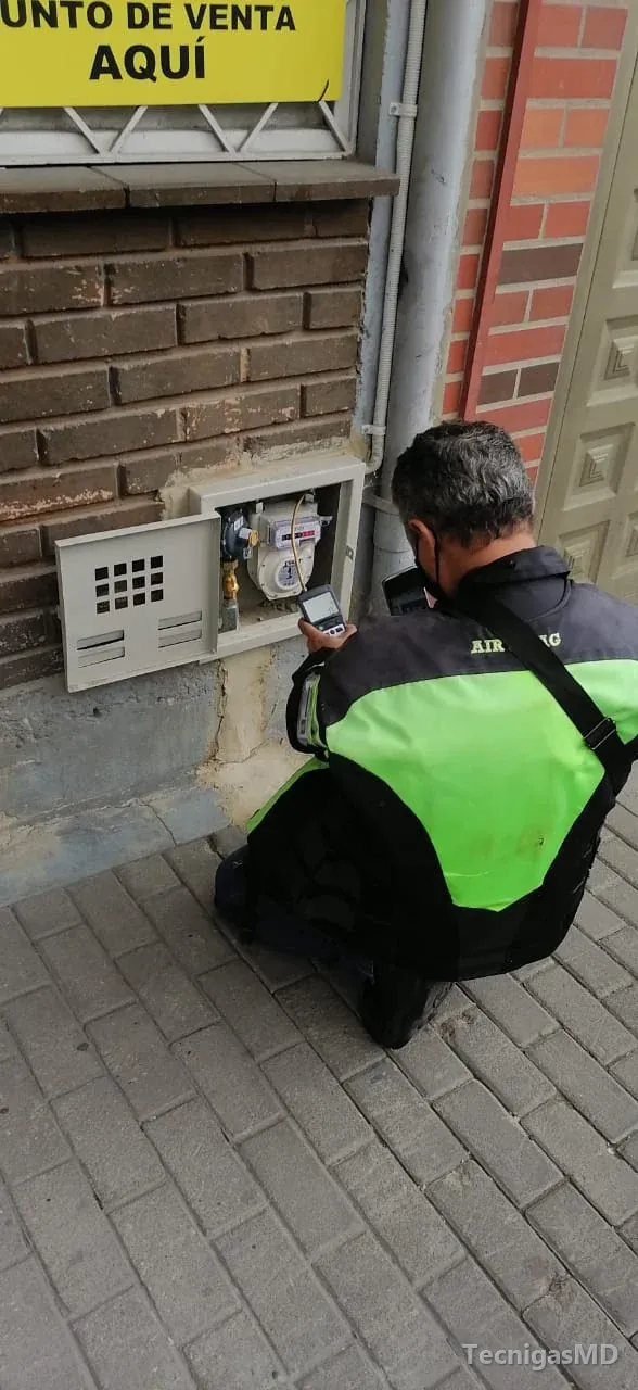 Técnico de TecnigasMD agachado frente al gabinete abierto de un medidor de gas natural, con un equipo de medición digital
