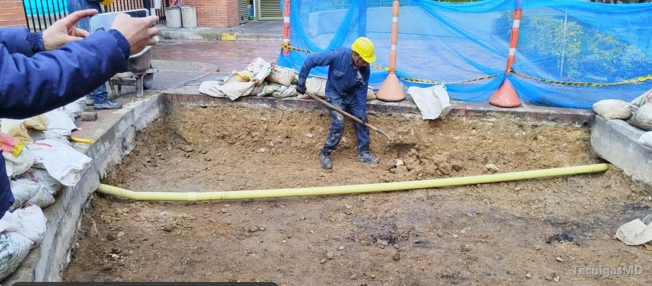 Técnico con casco y pala en la excavación donde quedó tendida la tubería amarilla de una acometida de gas natural