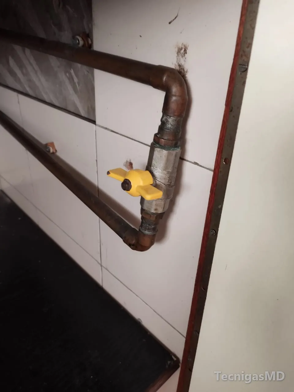 Tramo de tubería de cobre con válvula de paso de manija amarilla fijado a un muro enchapado en baldosa blanca